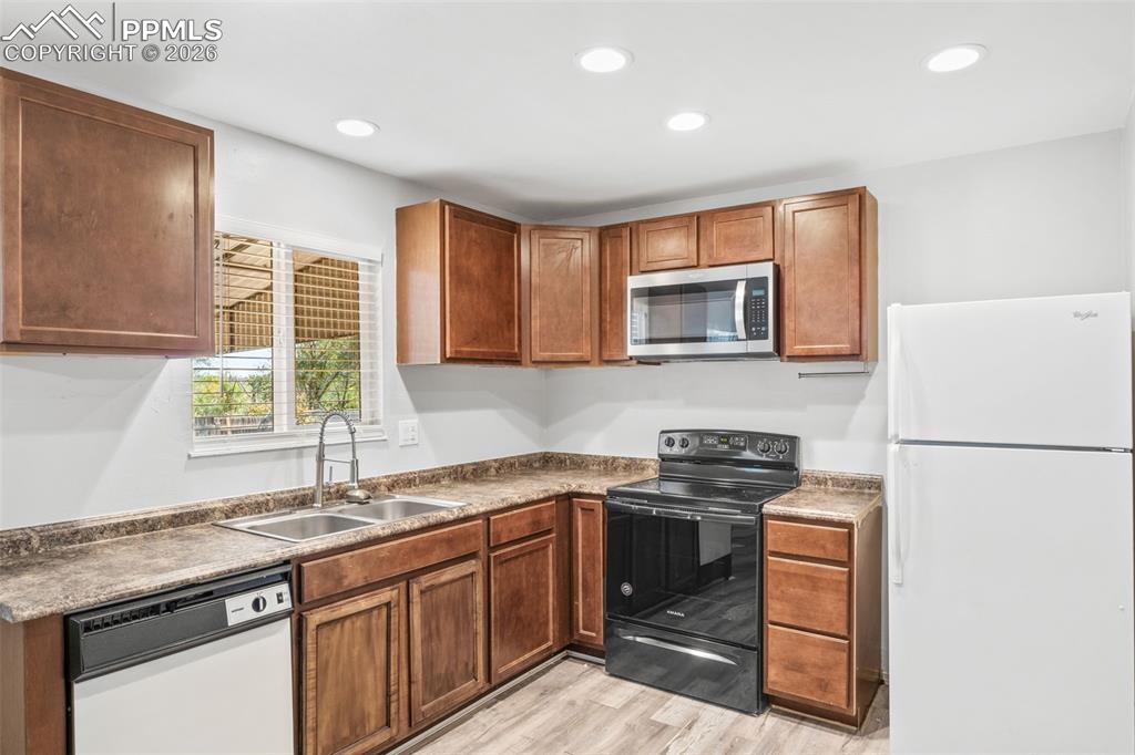 Kitchen featuring white appliances, wood finish cabinetry, light wood-style floors, recessed lighting, and dark countertops