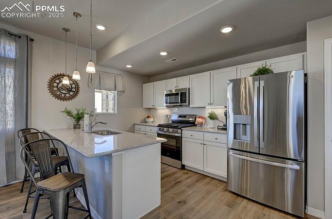 Kitchen featuring appliances with stainless steel finishes, a kitchen bar, light stone counters, white cabinets, and hanging light fixtures