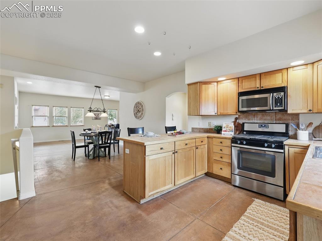 Kitchen featuring stainless steel appliances, finished concrete floors, a peninsula, recessed lighting, and light brown cabinets