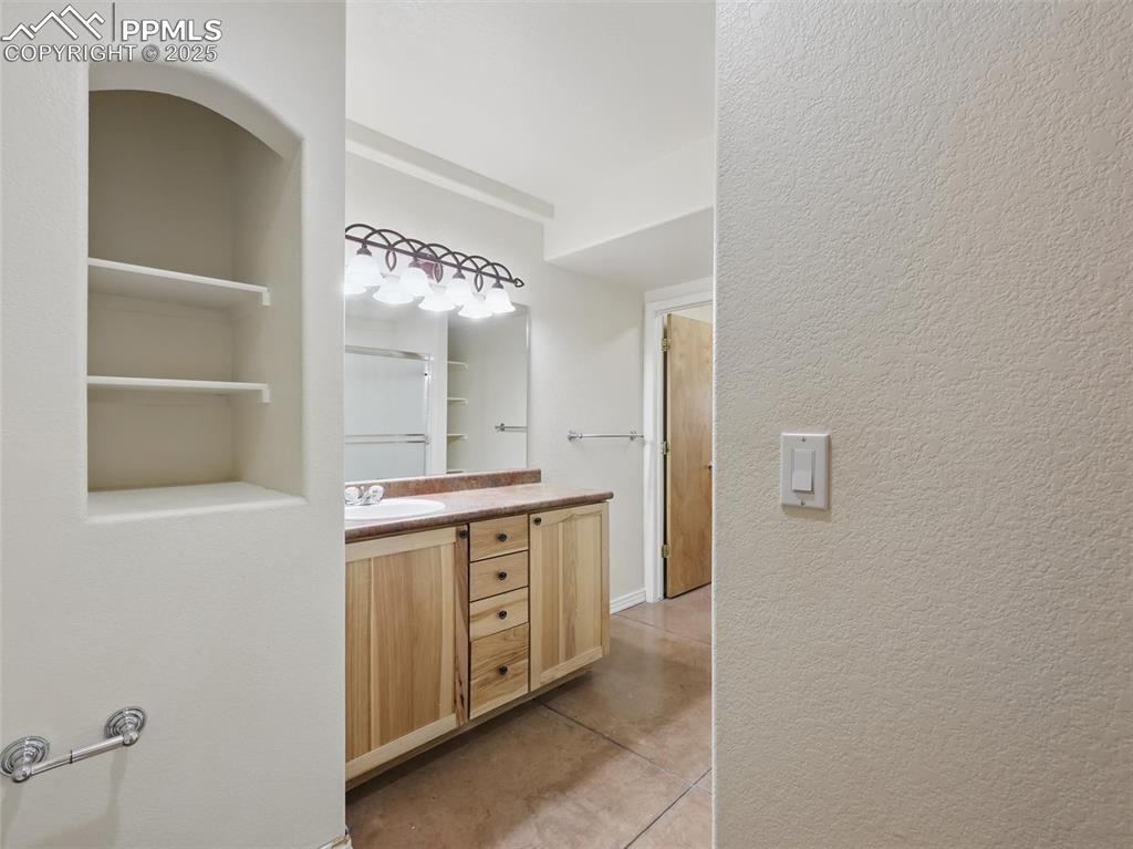 Bathroom with vanity, a textured wall, a shower, built in shelves, and light tile patterned floors