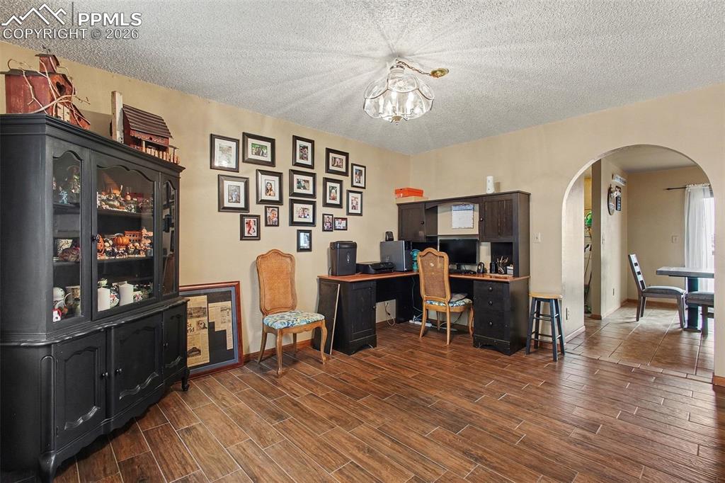 Office area with a textured ceiling, hanging lights, arched walkways, and wood tiled floors