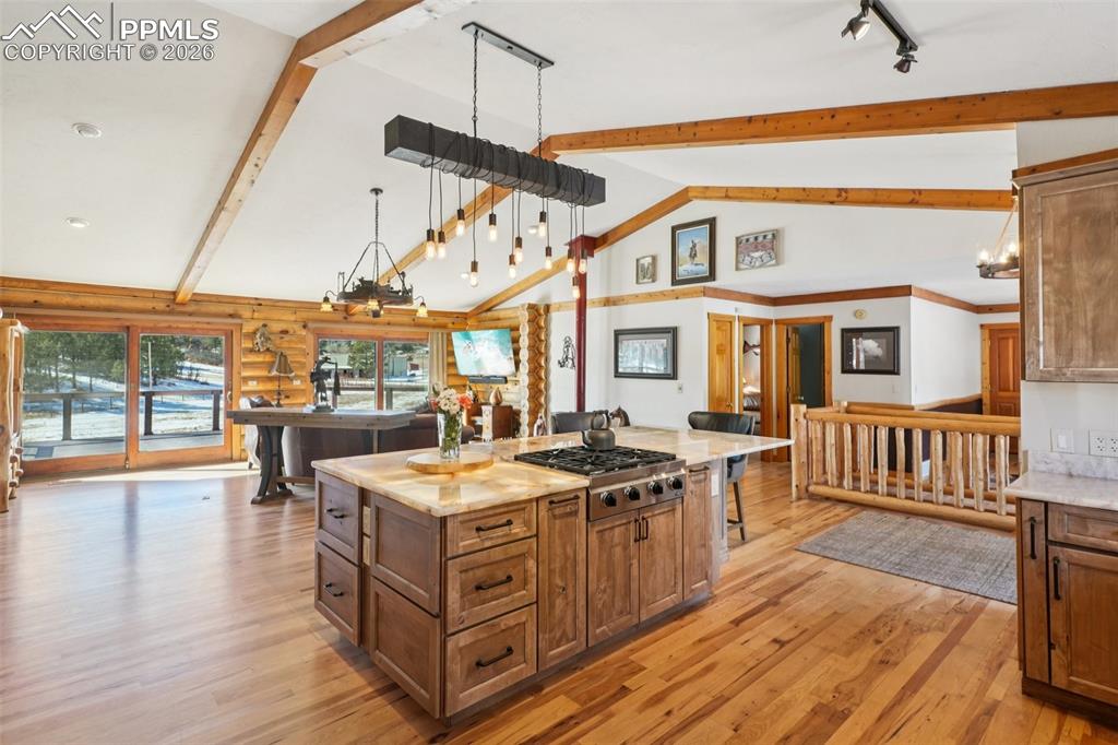 Kitchen with wood finish cabinets, light wood-type flooring, light stone countertops, a center island, and stainless steel gas stovetop