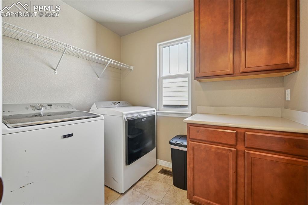 Laundry area featuring cabinet space, washer and dryer, a textured wall, and light tile patterned floors