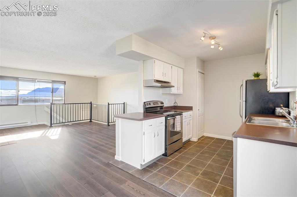 Kitchen with dark countertops, appliances with stainless steel finishes, white cabinets, under cabinet range hood, and dark wood finished floors