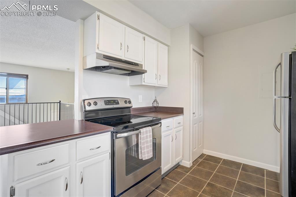 Kitchen featuring stainless steel appliances, white cabinetry, dark countertops, under cabinet range hood, and dark tile patterned floors