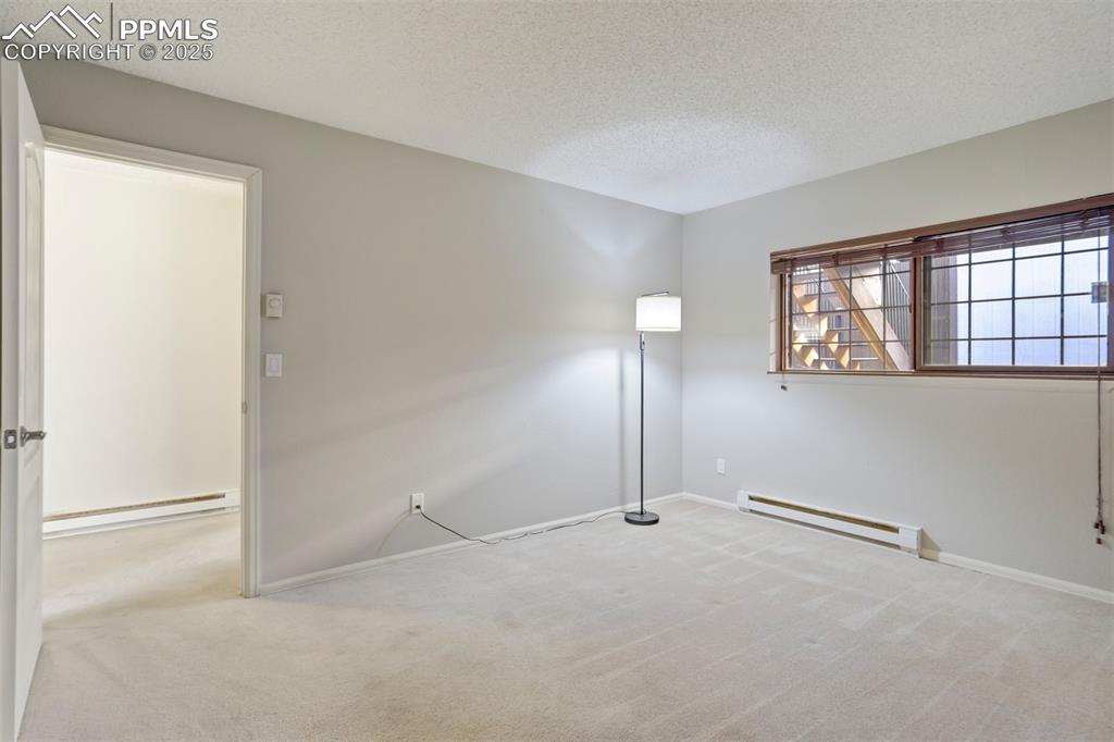 Spare room with a textured ceiling, light colored carpet, and a baseboard heating unit