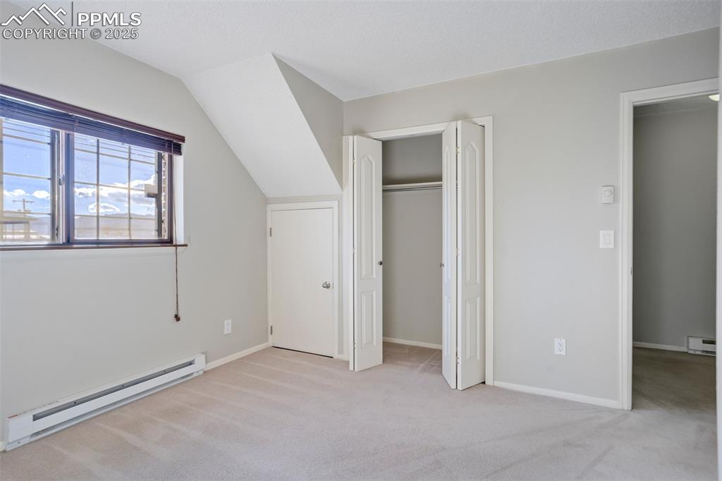 Unfurnished bedroom with a baseboard radiator, light colored carpet, a closet, a baseboard heating unit, and lofted ceiling