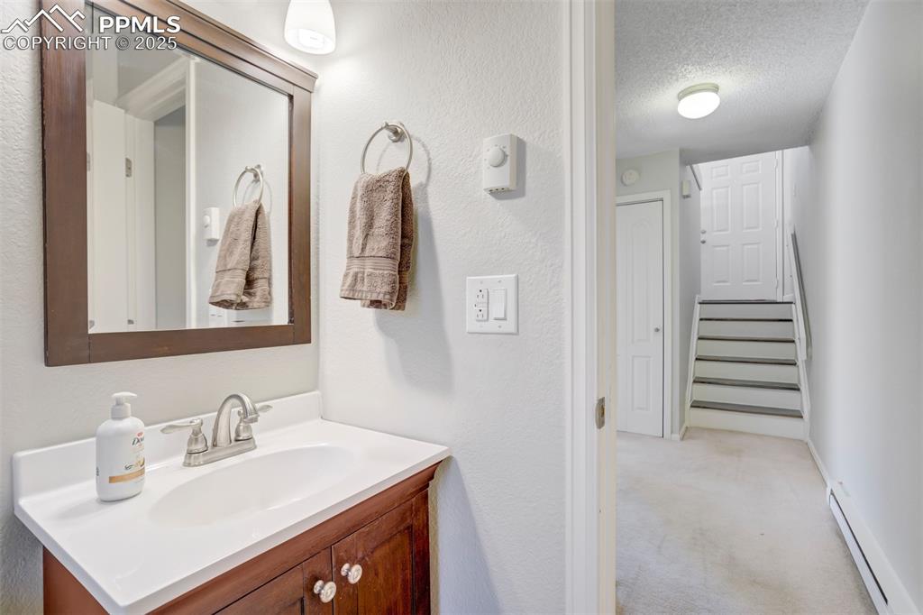 Bathroom featuring light colored carpet, a baseboard heating unit, vanity, a textured wall, and a textured ceiling