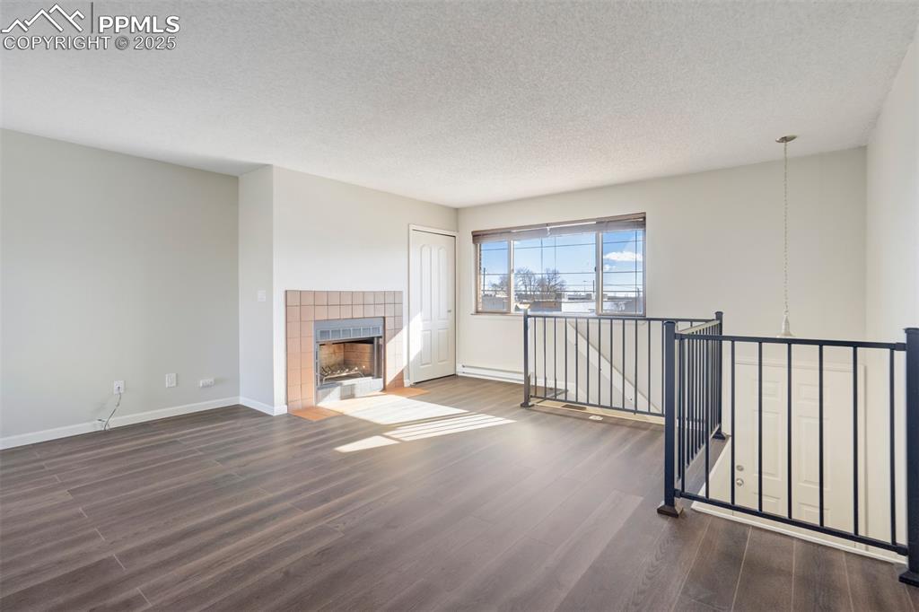 Unfurnished living room featuring dark wood-style flooring, a textured ceiling, and a tile fireplace
