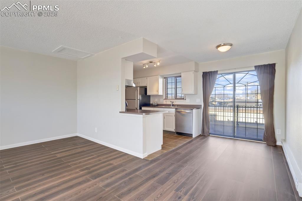Kitchen with white cabinets, dark wood-style floors, stainless steel appliances, a textured ceiling, and a peninsula