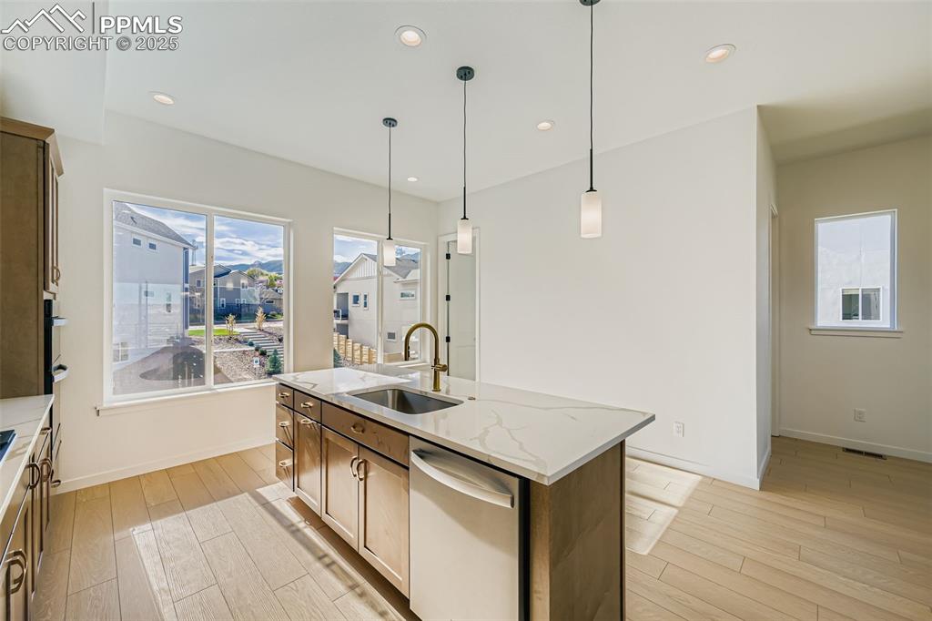 Kitchen with stainless steel dishwasher, recessed lighting, hanging light fixtures, light stone countertops, and light wood-style flooring