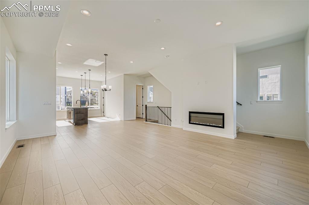 Unfurnished living room with a chandelier, recessed lighting, healthy amount of natural light, light wood-style floors, and a glass covered fireplace