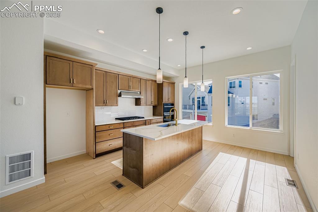Kitchen featuring pendant lighting, a kitchen island with sink, brown cabinetry, backsplash, and recessed lighting