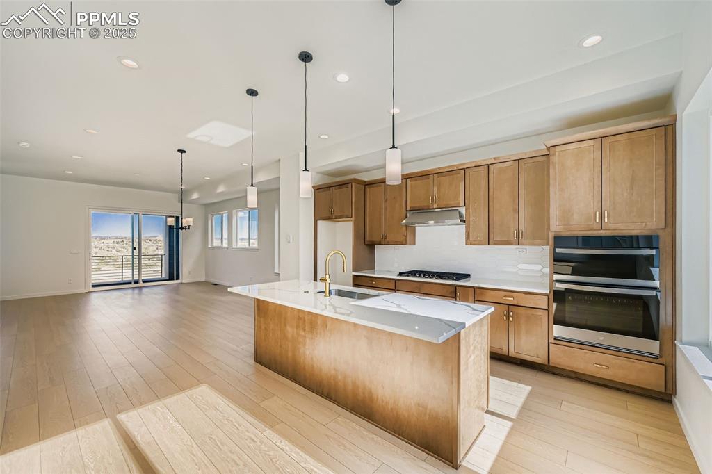Kitchen with decorative light fixtures, appliances with stainless steel finishes, recessed lighting, an island with sink, and light stone counters
