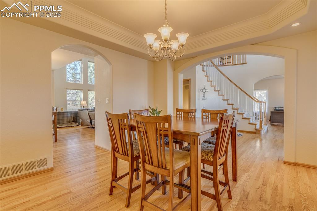 Dining area featuring light wood finished floors, hanging lights, a tray ceiling, crown molding, and plenty of natural light