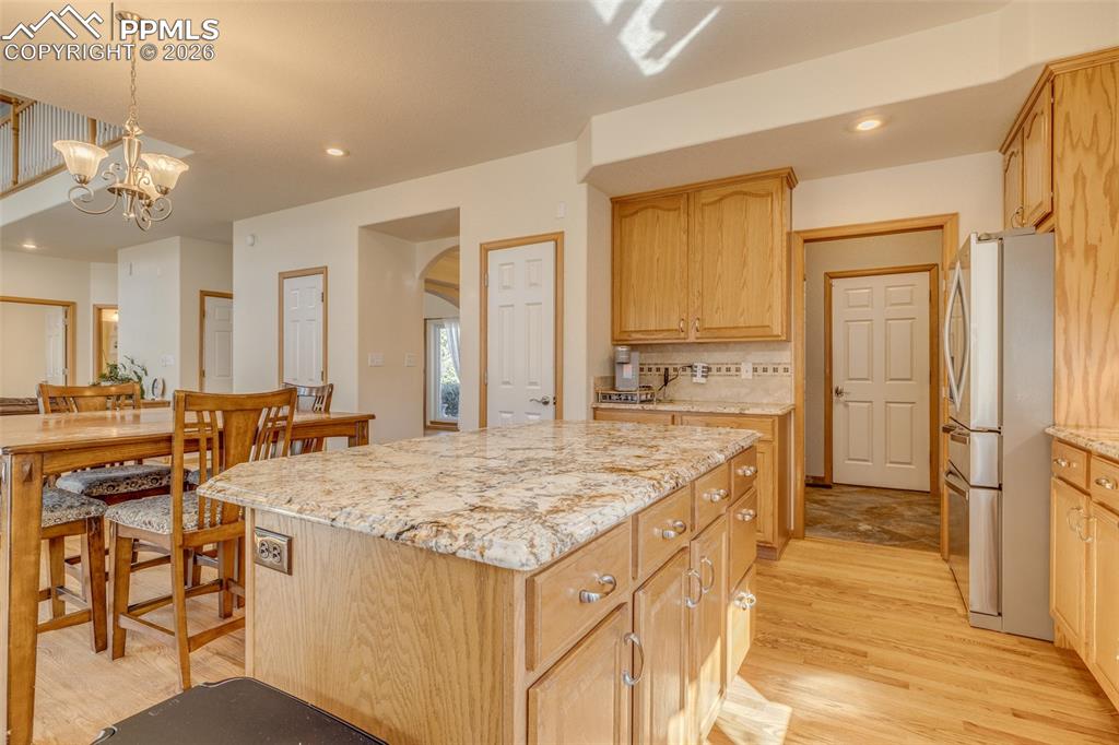 Kitchen featuring freestanding refrigerator, a center island, light wood-style flooring, tasteful backsplash, and light stone countertops