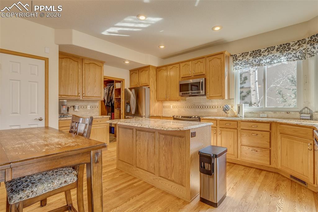 Kitchen with a kitchen island, light stone counters, stainless steel appliances, backsplash, and light wood finished floors