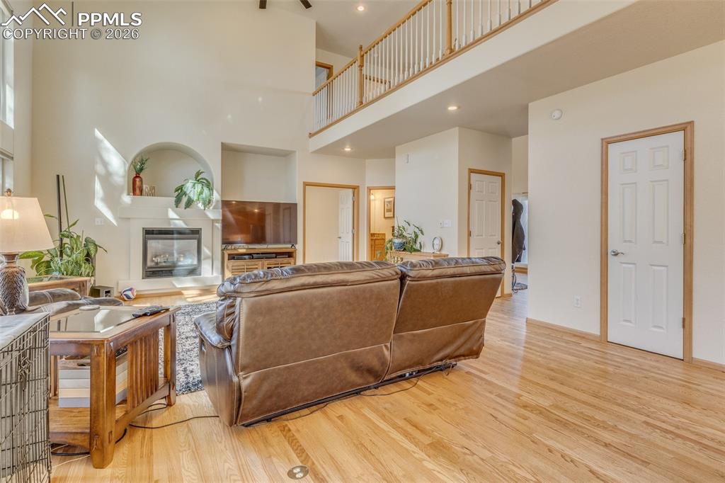 Living area with a glass covered fireplace, light wood-style floors, a high ceiling, and recessed lighting