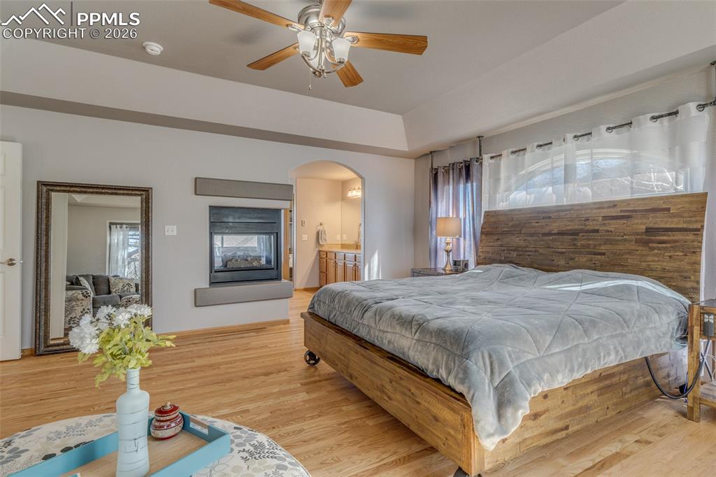 Bedroom with light wood-type flooring, multiple windows, a ceiling fan, and connected bathroom