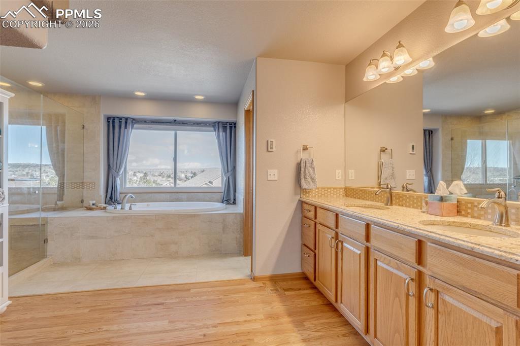 Full bathroom with double vanity, a shower stall, a bath, light wood finished floors, and recessed lighting