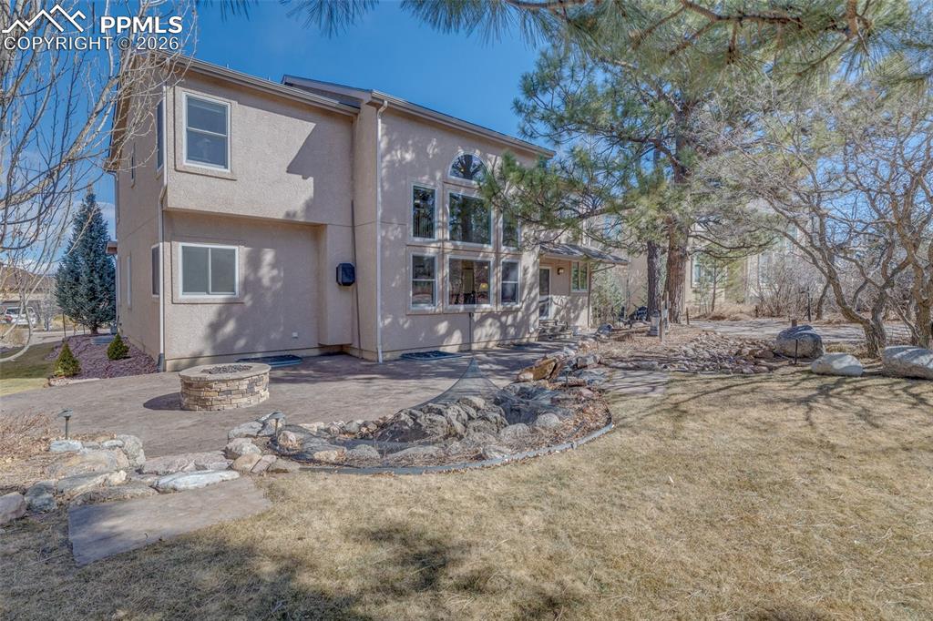 Rear view of house featuring a fire pit, stucco siding, a patio, and a lawn