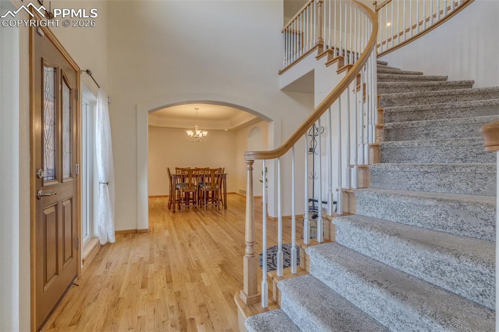 Entrance foyer featuring arched walkways, a high tray ceiling, light wood-style floors, and suspended lighting