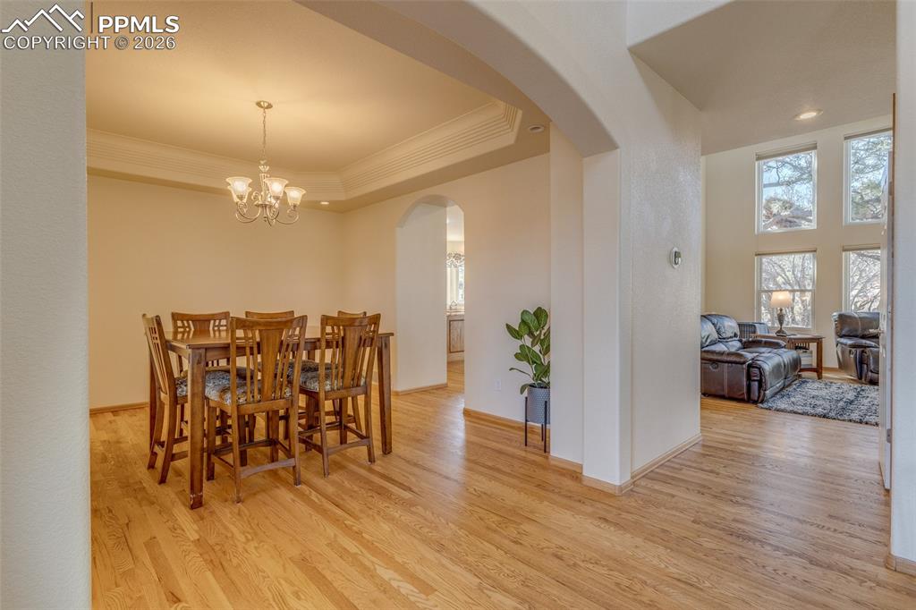 Dining room featuring light wood-style floors, crown molding, suspended lighting, arched walkways, and a tray ceiling