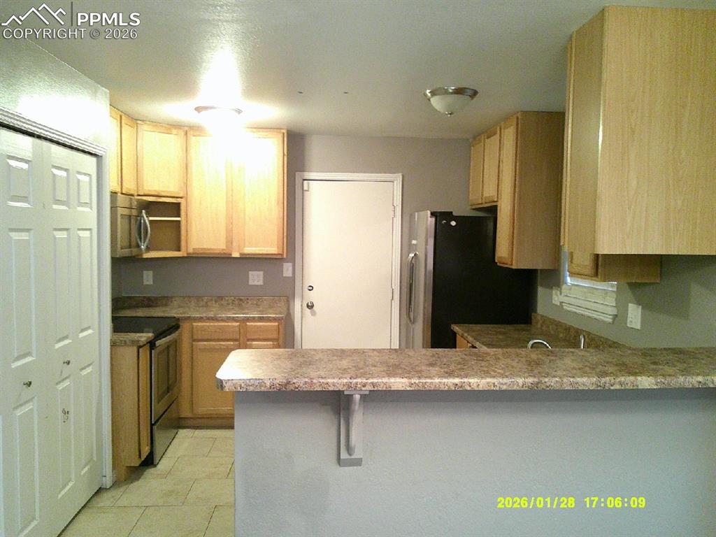 Kitchen featuring stainless steel appliances, light wood finish cabinets, a peninsula, a breakfast bar, and open shelves