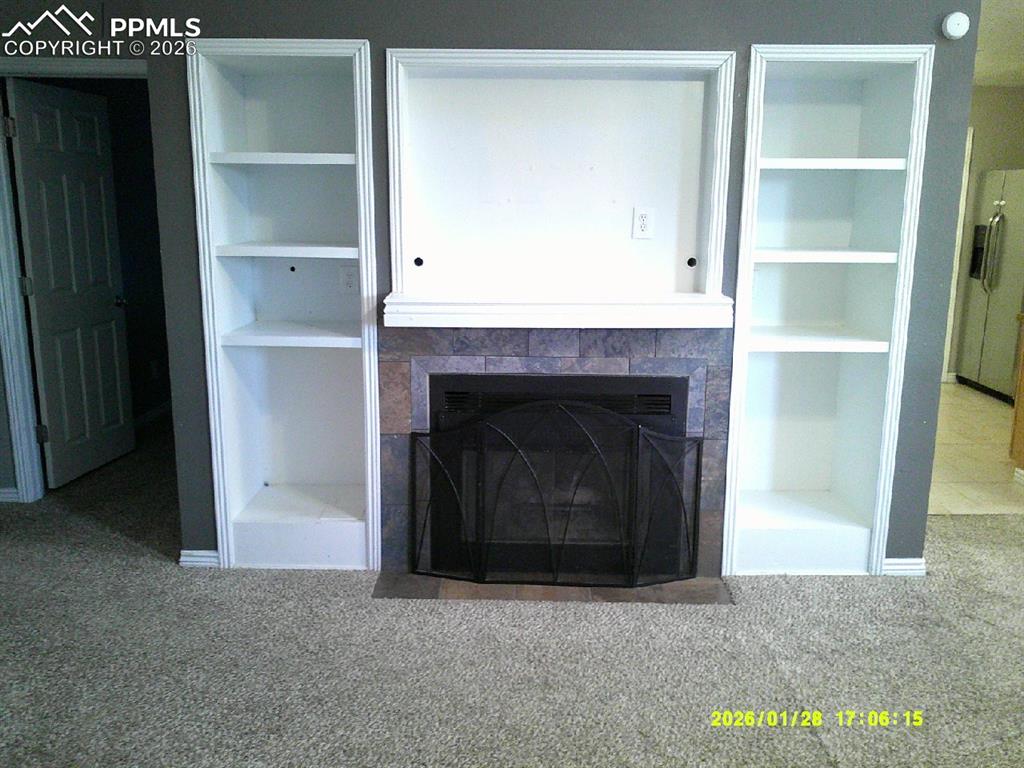 Detailed view of built in shelves, carpet flooring, fridge with ice dispenser, and a tiled fireplace