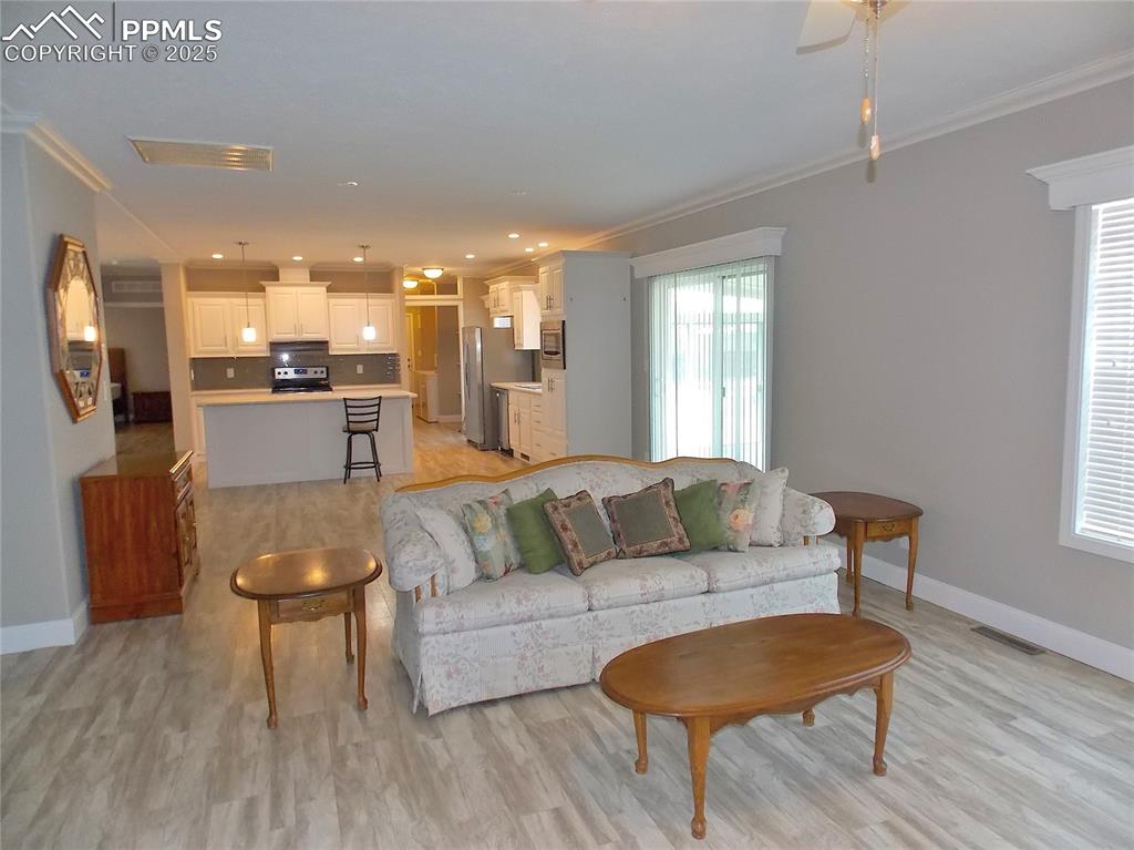 Living room with ceiling fan, light wood-type flooring, and ornamental molding