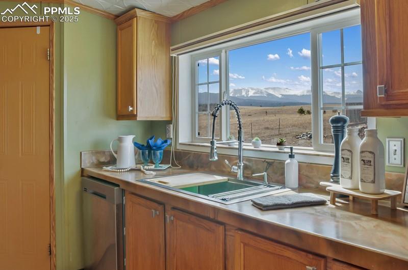 Kitchen with a mountain view, light countertops, brown cabinetry, dishwasher, and a sink