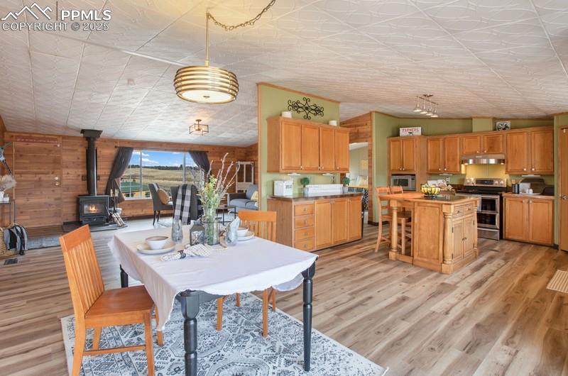 Dining area with light wood-type flooring, wood walls, a wood stove, and an ornate ceiling