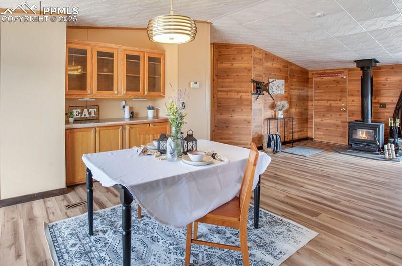 Dining area with baseboards, a wood stove, light wood-type flooring, vaulted ceiling, and wood walls