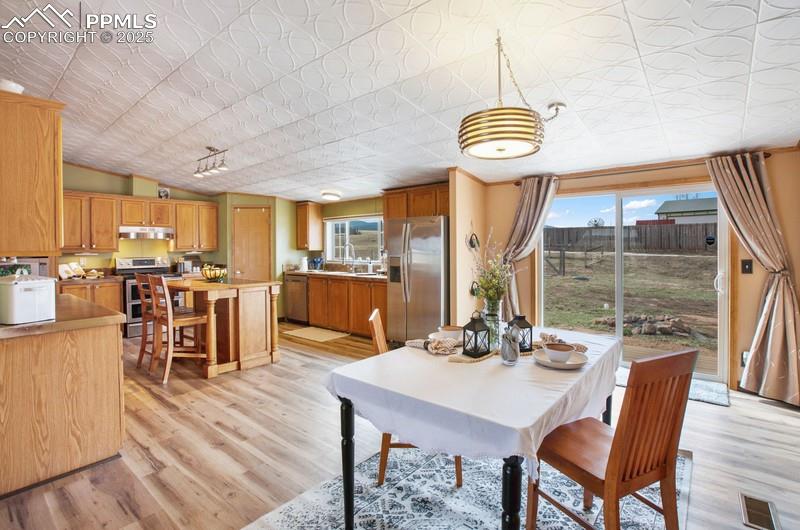 Dining area with light wood-style floors, an ornate ceiling, visible vents, and lofted ceiling