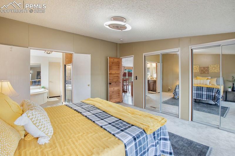 Bedroom featuring ensuite bath, light colored carpet, two closets, and a textured ceiling