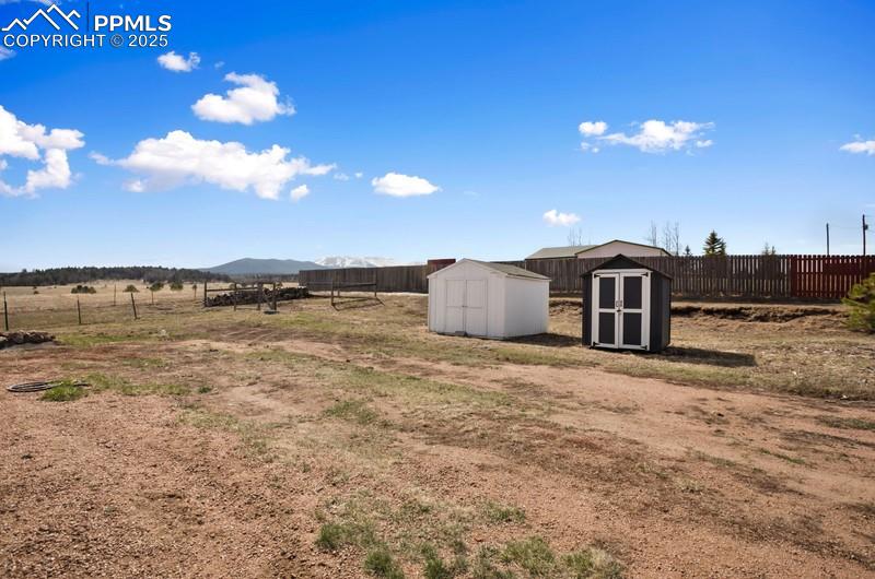 View of yard featuring a shed, a mountain view, fence, and an outbuilding