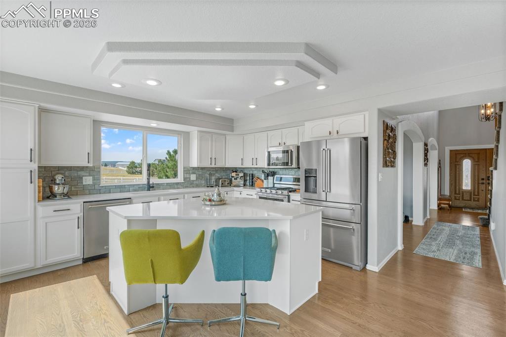 Kitchen featuring arched walkways, stainless steel appliances, white cabinetry, light wood-style floors, and a kitchen breakfast bar