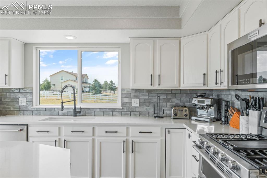 Kitchen featuring stainless steel appliances, light stone counters, white cabinets, and tasteful backsplash