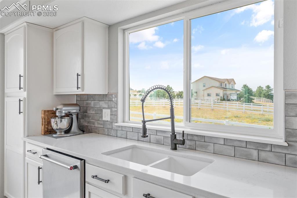 Kitchen featuring white cabinets, light stone countertops, stainless steel dishwasher, and decorative backsplash