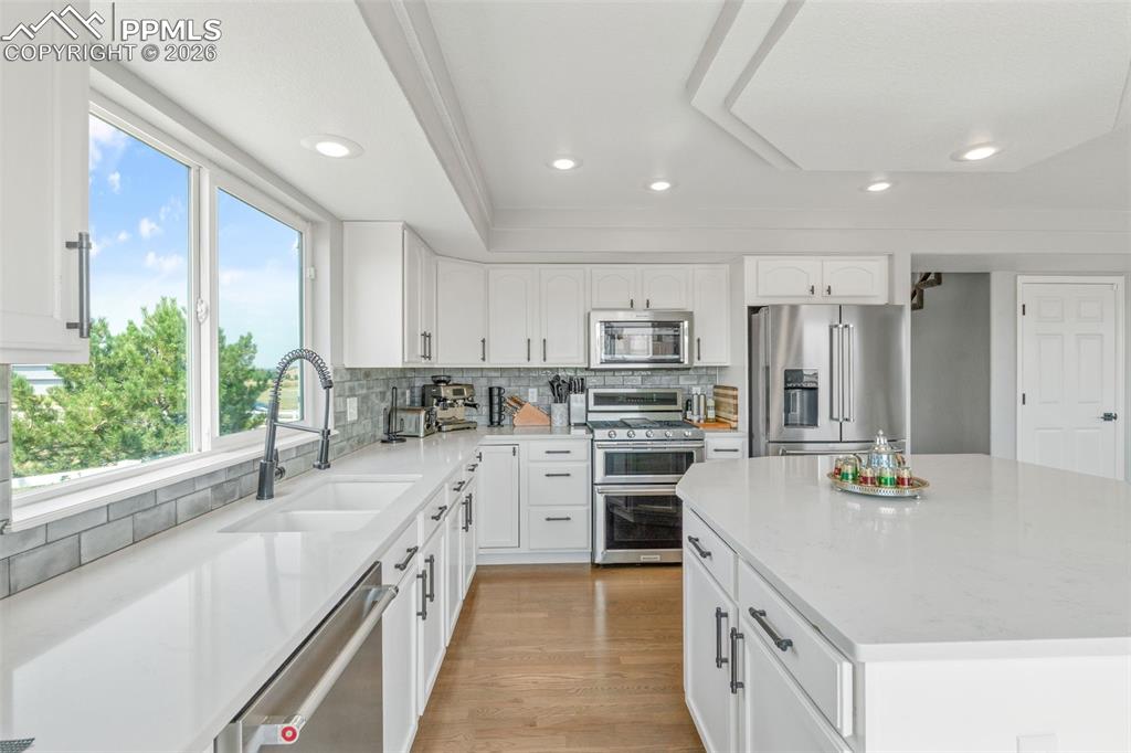 Kitchen with stainless steel appliances, a kitchen island, light wood-type flooring, light stone countertops, and white cabinetry