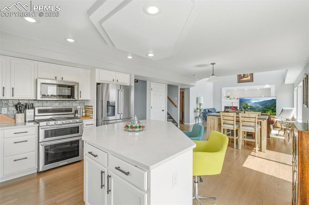 Kitchen featuring stainless steel appliances, light wood-style flooring, white cabinets, a center island, and backsplash