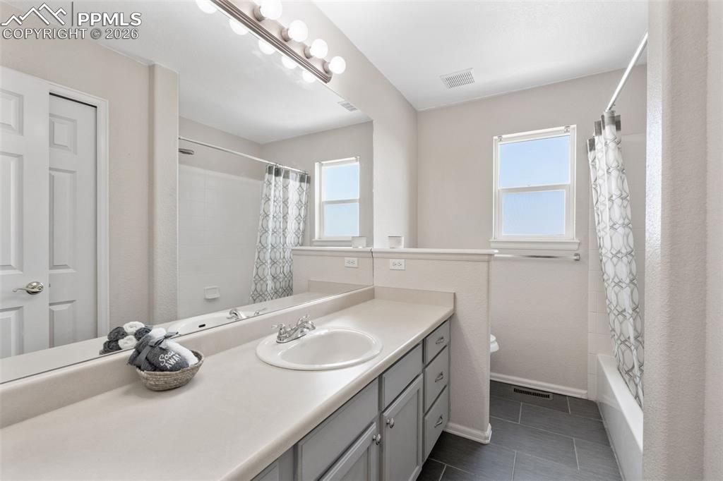 Full bathroom with vanity, shower / bath combination with curtain, dark tile patterned flooring, and plenty of natural light