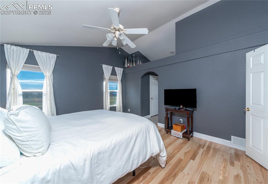 Primary Bedroom featuring lofted ceiling, light wood finished floors, a ceiling fan, and arched walkways