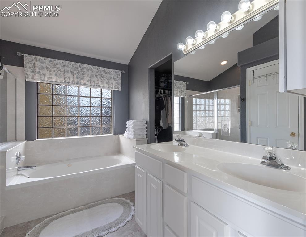 Full primary bath en suite with vaulted ceiling, a stall shower, a bath, double vanity, and a walk in closet
