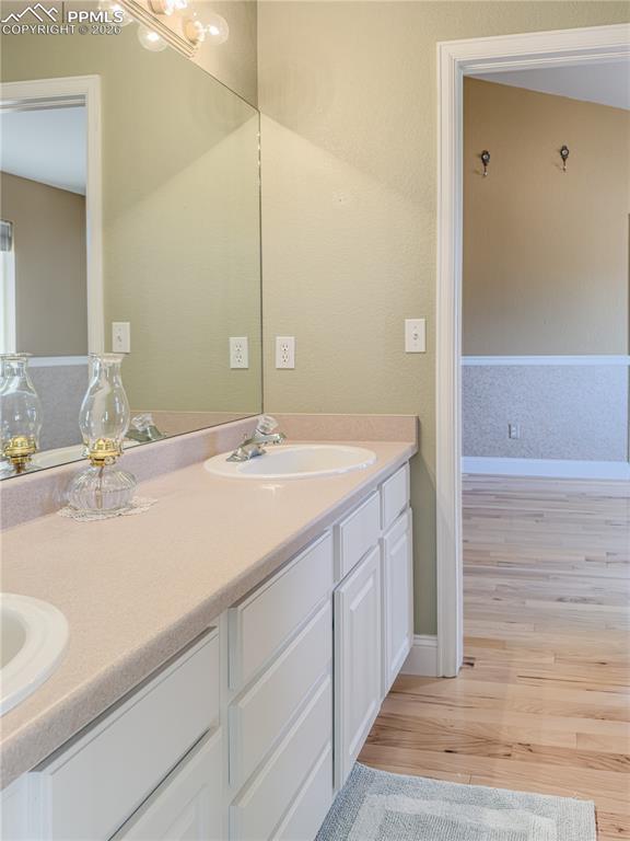 "Jack-and-Jill" Main-level Full Bathroom featuring a double vanity and light wood finished floors, enclosed entrance to water closet/shower/tub combo
