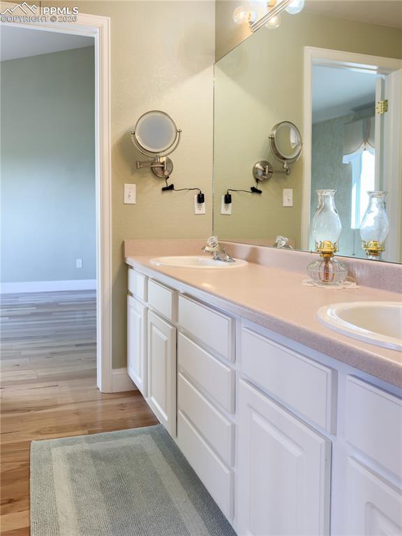 "Jack-and-Jill" Main-level Full Bathroom featuring a double vanity and light wood finished floors, enclosed entrance to water closet/shower/tub combo