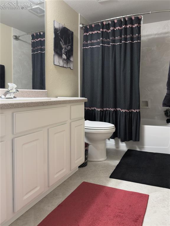 Basement-level Bathroom with vanity, shower / bathtub combination with curtain, and a textured wall