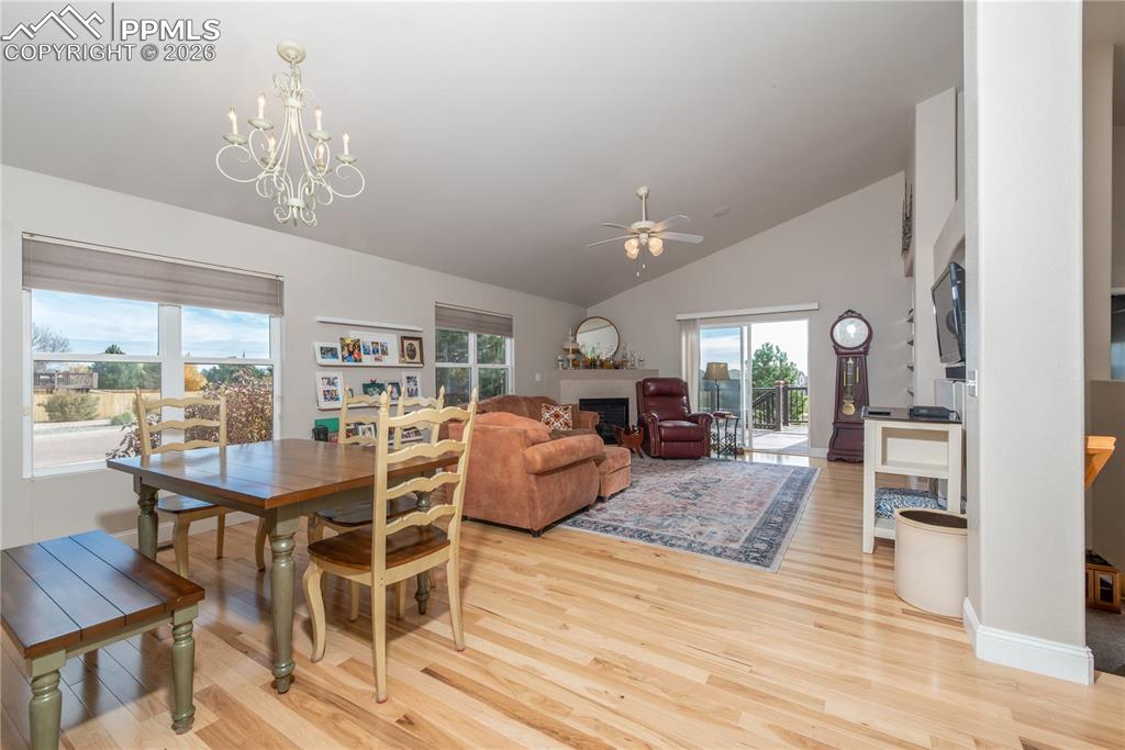 Dining area featuring light wood finished floors, ceiling fan, a chandelier, a fireplace, and high vaulted ceiling