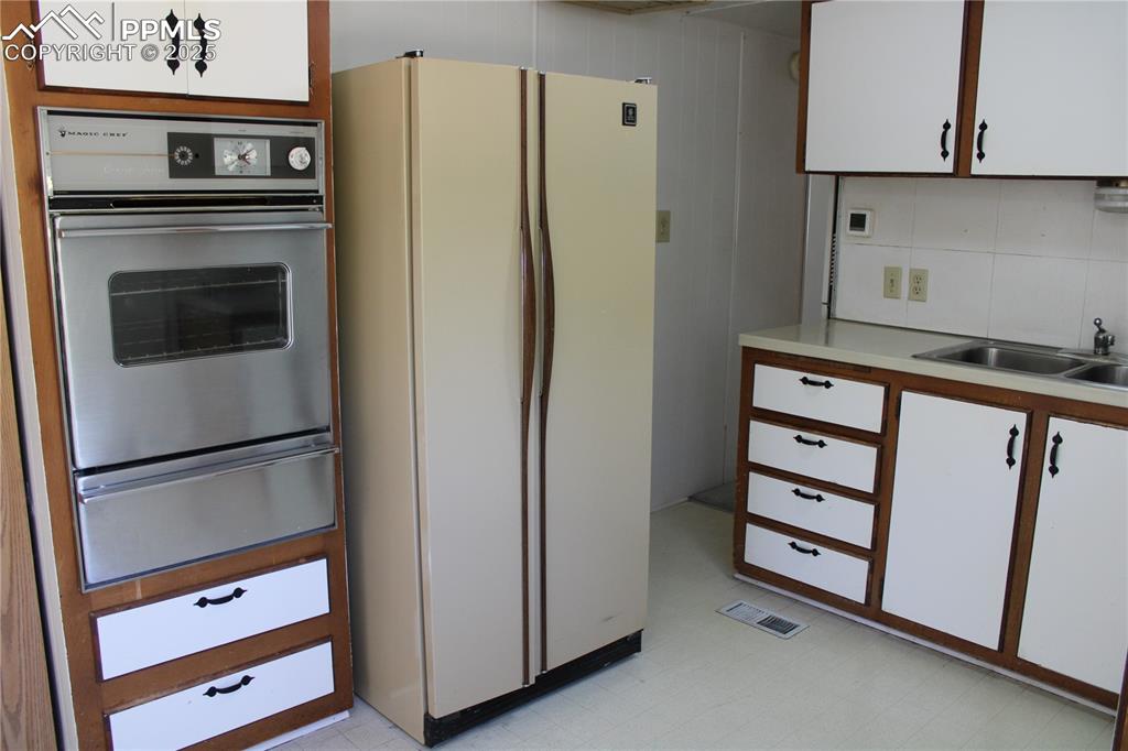 Kitchen featuring white cabinets, freestanding refrigerator, stainless steel oven, light countertops, and a warming drawer