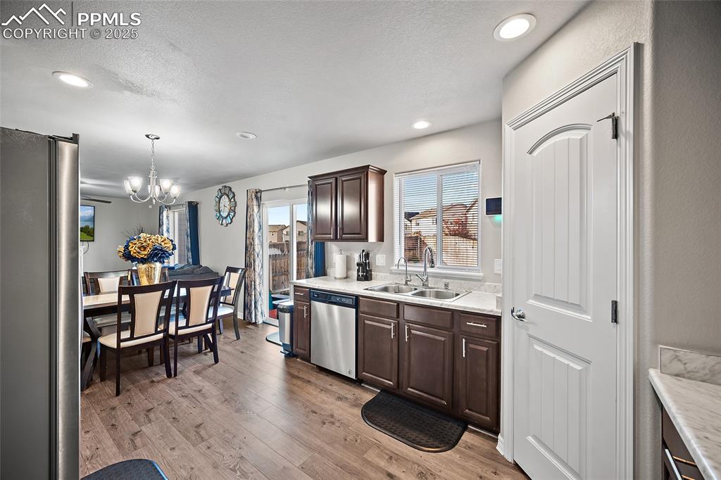 Kitchen featuring dark brown cabinets, stainless steel appliances, light wood finished floors, a chandelier, and decorative light fixtures